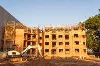 Site construction of unfinished wood framing multi-storey apartment complex, excavator on base engineering, concrete garage-wrap, pile of debris/sand. Multifamily/student housing project in Texas, USA